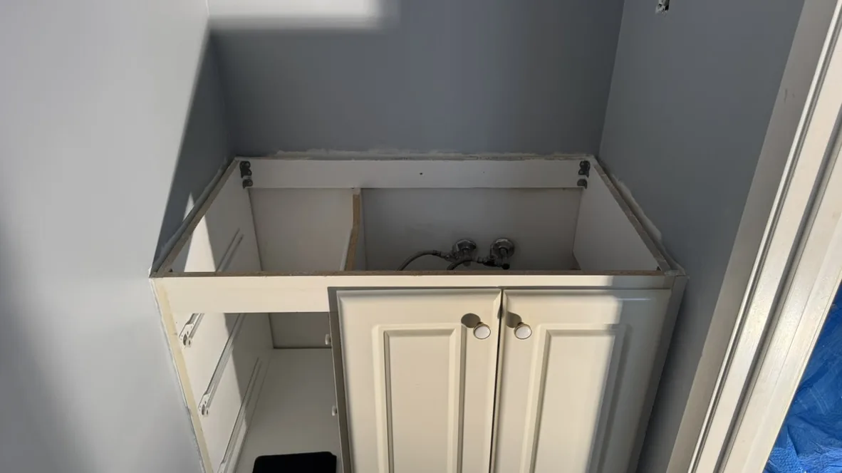 An existing white bathroom vanity cabinet in a wall-to-wall alcove with the old top off and the plumbing showing, Aurora Ontario