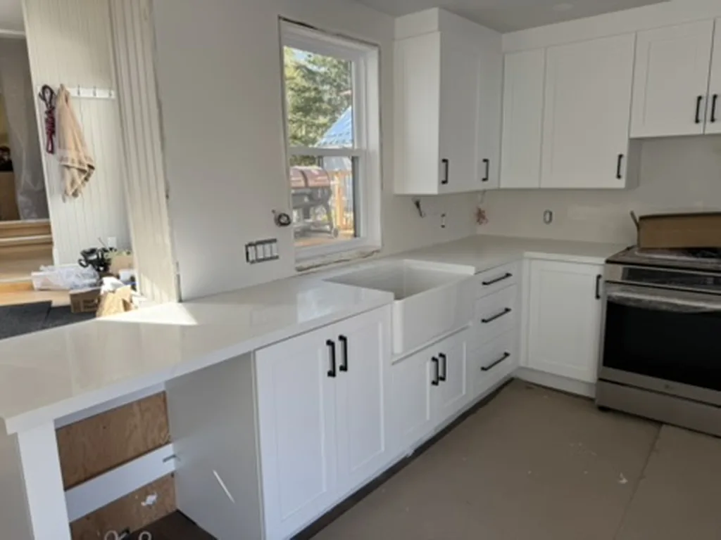 The same wall finished with white shaker cabinets, white quartz counters, a white farmhouse sink under the window and a slide-in range, Schomberg Ontario