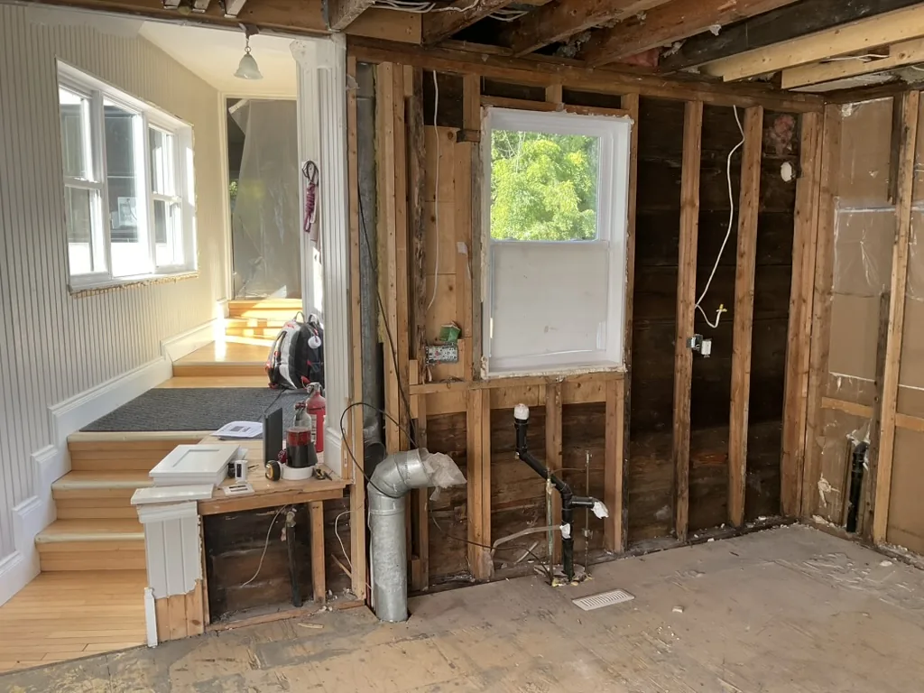 The sink wall of a Schomberg kitchen stripped to the studs, with the drain and vent pipes exposed under the window